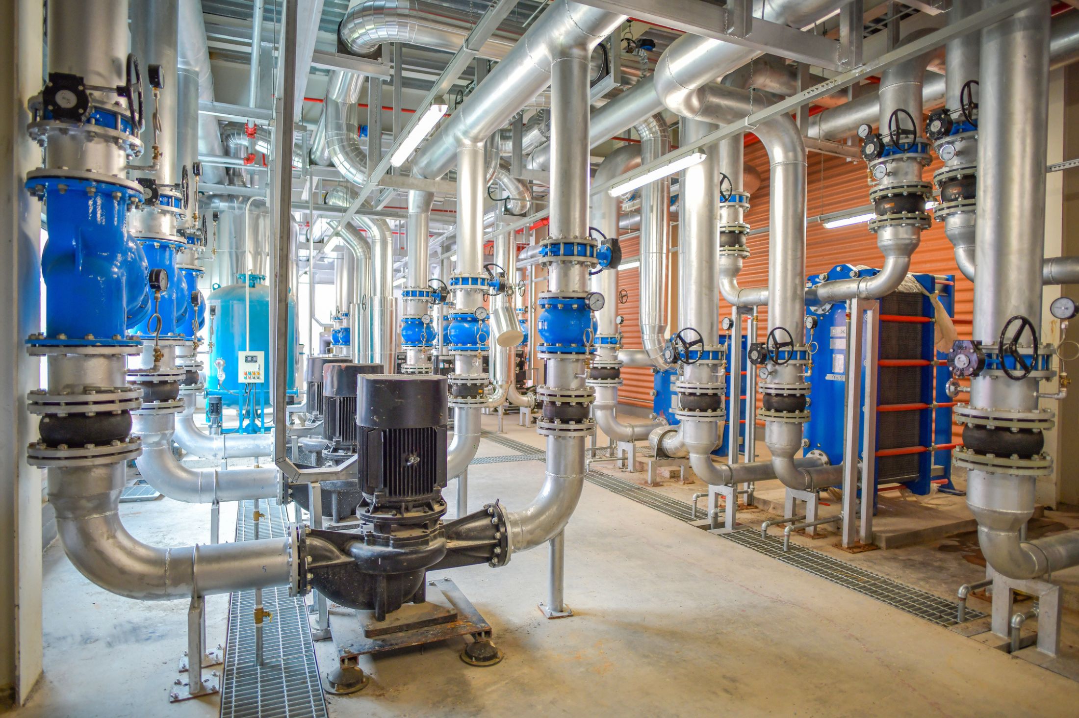 An industrial facility with interconnected metal pipes, valves, and large pumps, designed for fluid or gas distribution.